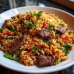 Close-up van een witte kom gevuld met smakelijke Steak Fried Rice, stukjes rundvlees en groene groenten.