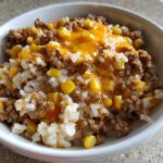 Close-up of a white bowl filled with Mexican Beef and Rice Skillet, featuring ground beef, white rice, corn, and melted cheddar cheese.