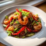 A vibrant plate of Soba Noodle Salad With Shrimp, garnished with sliced red bell peppers and green onions.