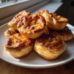 A stack of freshly baked Apple Cheddar Puff Pastry Bundles with golden, flaky crusts.