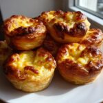 A stack of freshly baked Apple Cheddar Puff Pastry Bundles with golden, cheesy tops.