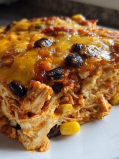 A close-up slice of baked Chicken Enchiladas Casserole topped with melted cheese, black beans, and corn.