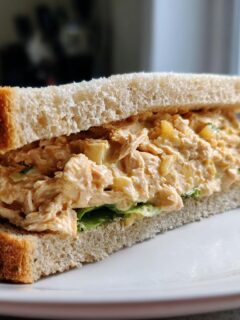 A close-up of a hearty Chicken Pineapple Sandwich, featuring shredded chicken salad with visible pineapple chunks between two slices of white bread.