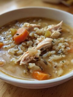 Close-up of a white bowl filled with creamy Chicken Wild Rice Soup, featuring shredded chicken, carrots, and mixed rice.