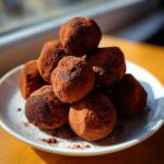 A tempting pile of homemade Classic Chocolate Truffles heavily dusted with dark cocoa powder, resting on a white plate.