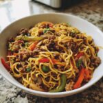 A close-up of a white bowl filled with savory Ground Chicken Chinese noodles mixed with colorful bell peppers and mushrooms.