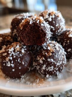 A close-up of rich, dark chocolate Salted Caramel Fudge Truffles topped with flaky sea salt.