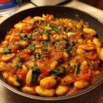 Close-up of a rich, red sauce featuring white beans and greens, garnished with parsley, served hot in a black skillet, representing the Tuscan White Bean Skillet.