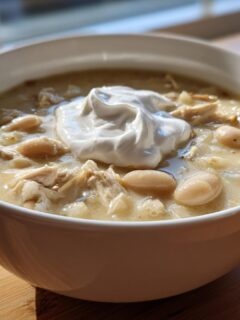 A close-up of a white bowl filled with creamy White Chicken Chili, topped with a dollop of sour cream.