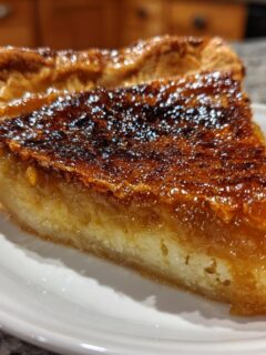 A close-up of a thick slice of Salted Honey Pie featuring a deeply caramelized, glossy top and flaky crust.